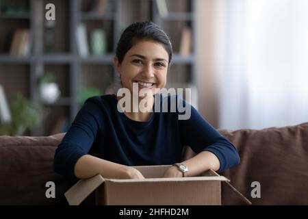 Porträt einer glücklichen jungen indischen Frau, die Karton auspackt. Stockfoto