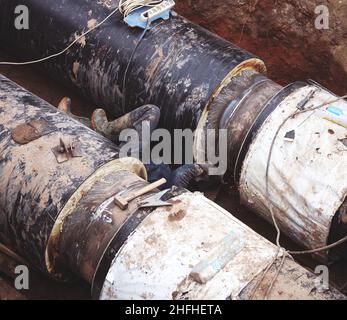 Reparatur des Heizkanals. Die Arbeiter, Schweißer, die durch Elektroschweißen und Gasschweißen an großen Eisenrohren in einer Tiefe von ausgegrabenen Graben hergestellt wurden. Stockfoto