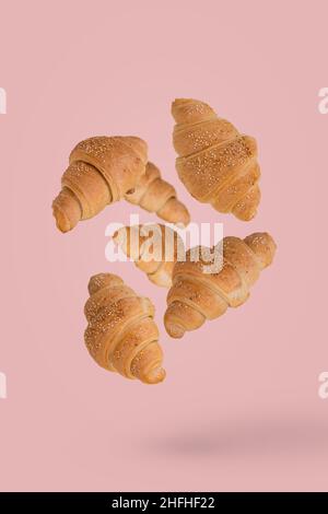 Frisch gebackene Croissants fliegen in der Luft isoliert auf einem pastellrosa Hintergrund. Kreatives Frühstückskonzept. Stockfoto