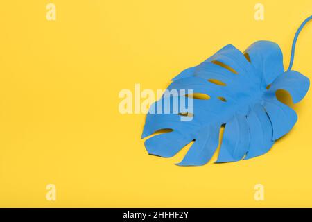 Tropisches Palmenblatt aus Monstera in blauer Farbe auf gelbem Hintergrund. Konzeptkunst. Minimalismus und Surrealismus. Speicherplatz kopieren. Stockfoto