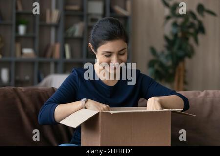 Neugierige lächelnde tausendjährige indische Frau Auspacken Karton. Stockfoto