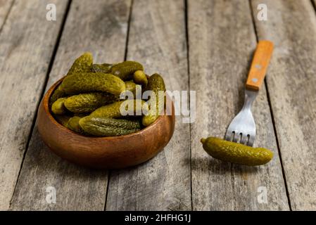 Schüssel mit eingelegten Gurken und Gabel mit Gurke auf einem rustikalen Holztisch. Stockfoto