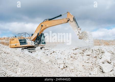 Bagger mit großem Eimer schüttet Gestein in eine tragbare Zerkleinerungsanlage auf der Baustelle oder im Steinbruch. Bergbau schwere Maschinen Details Stockfoto