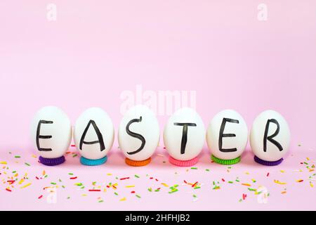 Weiße Eier mit schwarzen Buchstaben OSTERN und süße Farbe streut auf einem rosa Hintergrund. Frohe Ostern Karte. Flach liegend, Draufsicht, Kopierbereich. Stockfoto