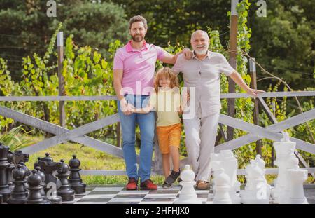 Portrait von Großvater Vater und Sohn spielen Schach. Glückliche Männer in verschiedenen Altersgruppen spielen Schachbrettspiel. Drei-Mann-Generation. Stockfoto