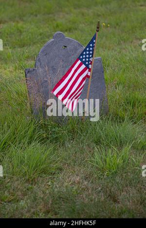 Eine amerikanische Flagge fliegt neben einem Grabstein auf dem Center Cemetery, New Salem, MA Stockfoto