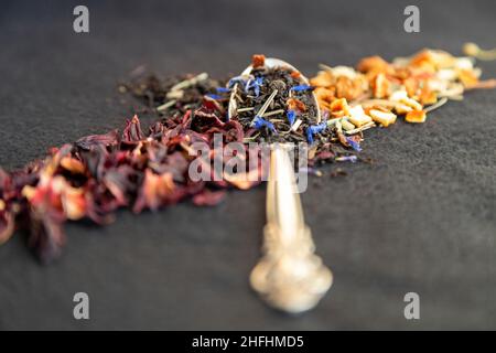 Tee. Guten Morgen. Metalllöffel, auf dem der Tee diagonal ausgelegt ist, verschiedene Teesorten, schwarz, Obst, grün. Vorderansicht. Stockfoto