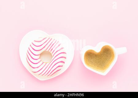 Kaffeetasse und rosa Donut in Herzform Teller. Valentinstag-Konzept. Draufsicht, Platz für Text kopieren. Stockfoto