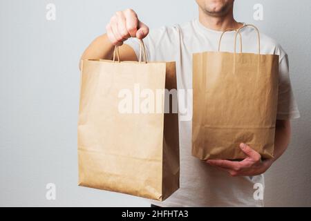 Lieferkonzept - schöner kaukasischer Liefermann, der eine Packtasche mit Lebensmitteln und Getränken aus dem Laden trägt. Isoliert auf grauem Studiohintergrund. Kopieren Stockfoto