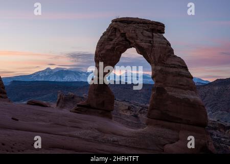 Morgenfarbe über dem zarten Bogen mit den schneebedeckten La Sal Bergen in der Ferne im Arches National Park Stockfoto