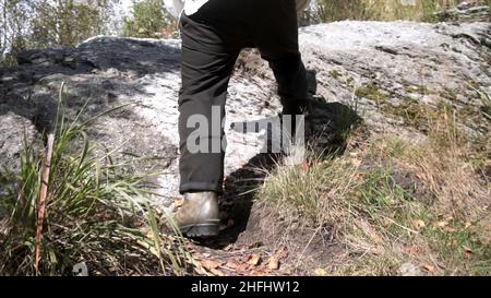 Nahaufnahme von Mann Gummistiefeln beim Wandern auf dem Trail in den Bergen in verdorrten Gras. Wanderer Mann Beine Klettern den steilen Hang des Felsens Stockfoto