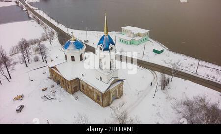 Luftaufnahme über die weiße Kirche im Winter bei starkem Schnee. Luftaufnahme der Kirche in Russland. Clip. Kleine Stadtkirche im verschneiten Winter in einem kleinen Schlepptau Stockfoto