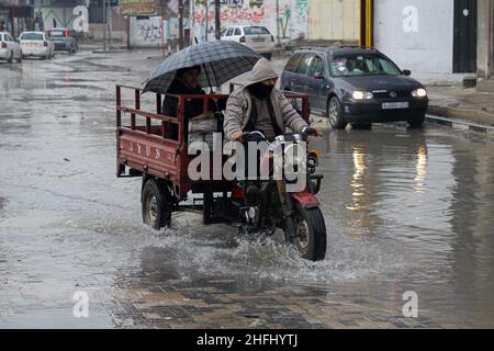 Gaza. 16th Januar 2022. Ein Palästinenser fährt am 16. Januar 2022 mit einem motorisierten Dreirad durch eine überflutete Straße nach sintflutartigen Regenfällen im Flüchtlingslager Jabalia im nördlichen Gazastreifen. Kredit: Rizek Abdeljawad/Xinhua/Alamy Live Nachrichten Stockfoto