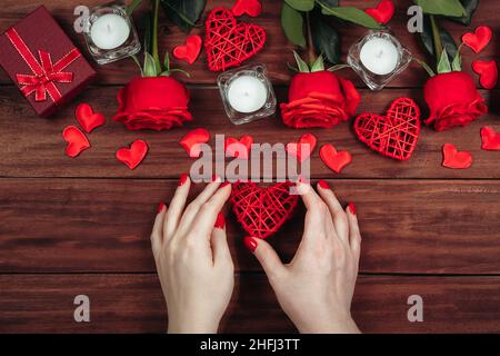 Die Hände der Frauen halten das Herz. Valentinstag-Konzept. Rote Rosen und Kerzen auf Holzgrund. Stockfoto