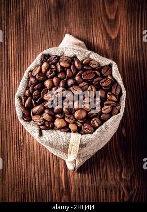 Sackleinen mit Kaffeebohnen auf Holzhintergrund Stockfoto