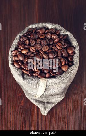 Sackleinen mit Kaffeebohnen auf Holzhintergrund Stockfoto