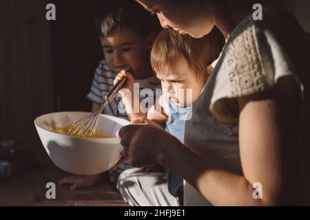 Kinder, die Mehlpulver in einer Schüssel durchsieben, Teig mischen und schlagen. Familientag. Stockfoto