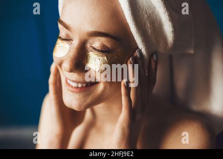 Nahaufnahme Porträt einer Sommersprossen Frau mit Handtuch auf dem Kopf Verwenden Sie Gesichtsfarbe goldene Augen Patch für die Haut. Schönheitsbehandlung. Beauty Mode Modell. Beauty Face Stockfoto