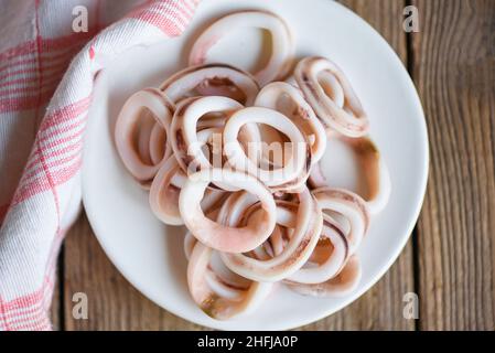 Tintenfischringe auf weißem Teller, frischer Tintenfisch gekocht mit Salat für Lebensmittel auf Holzboden Stockfoto
