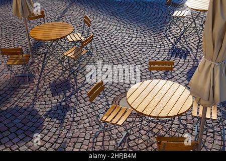 Im Freien können Gäste in einem deutschen Café mit runden Tischen und Holzstühlen sitzen Stockfoto