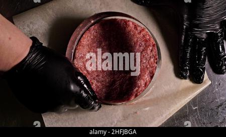 Kochen macht Fleisch Medaillons für Burger. Koch in schwarz Handschuhe macht Schnitzel essen. Die koteletts sind in Stahl Ring in eine noch Medaillon eingeebnet. Stockfoto