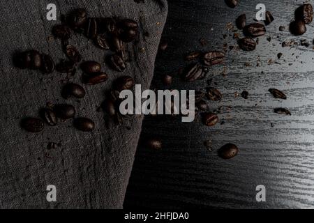 Verschüttete Kaffeebohnen auf schwarzem Holztisch und grauem Stoff Stockfoto
