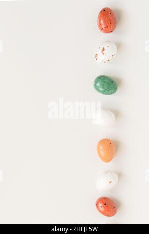 Ostern minimale Zusammensetzung mit bunten Eiern auf dem weißen Hintergrund. Osterkonzept. Platz zum Kopieren, flach liegend. Vertikales Foto. Stockfoto
