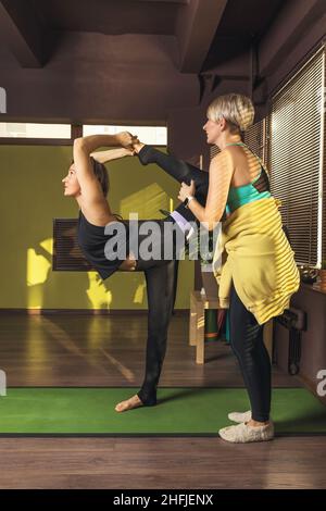 Die Trainerin hilft den Studenten bei der Durchführung der Natarajasana-Übung, der Pose des Königs der Tänzer, der im Studio auf der Matte steht Stockfoto