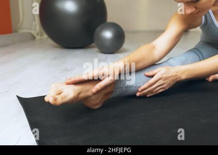 Eine Frau führt eine Knöcheldehnung durch, sitzt auf einer Gymnastikmatte im Studio Stockfoto
