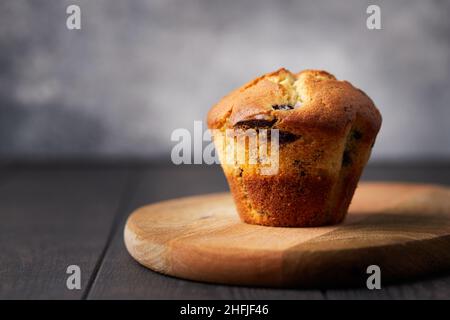 Muffin mit Schokolade und Heidelbeeren auf einem Holzständer auf dunklem Hintergrund. Vorderansicht. Stockfoto