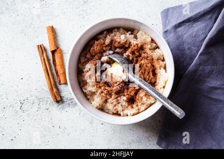 Skandinavischer Reisbrei mit Zimt und Butter in einer weißen Schüssel auf grauem Hintergrund, Draufsicht. Norwegisches Küchenkonzept. Stockfoto