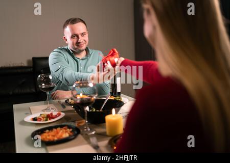 Zwei verliebt zu Hause zu Abend essen, gibt eine Frau einem Mann ein Überraschungsgeschenk für einen Jahrestag oder valentinstag, Hochzeit Jubiläumsfeier, romantisch Stockfoto