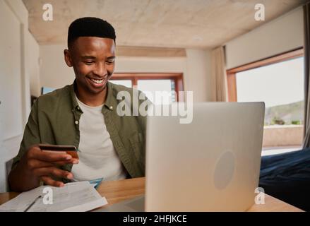 Junge Erwachsene schwarze Männer aufgeregt, Online-Kauf auf Laptop in einer modernen Wohnung zu machen. Stockfoto