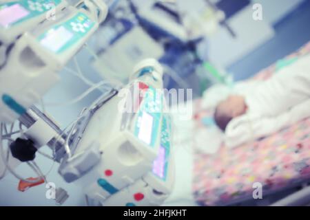 Neugeborenes Baby auf dem Bett, umgeben von der Ausrüstung auf der Intensivstation des Kinderkrankenhauses. Stockfoto