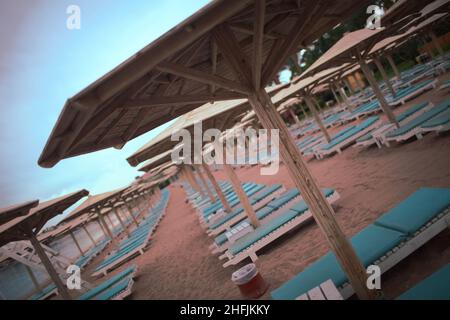 Leerer Strand mit Sonnenschirmen und Sonnenliegen aus Holz. Stockfoto