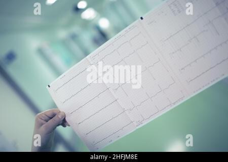 Eine Ärztin, die das EKG des Patienten untersucht, führt zu einem langen Krankenhausflur. Stockfoto