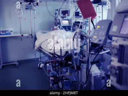 Kritisch erkrankte komatöse Patientin im Krankenhausbett, verbunden mit der fortgeschrittenen Lebenserhaltungs-Ausrüstung auf der Intensivstation, unfokussierter Hintergrund. Stockfoto