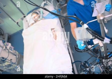 Krankenschwester, die den Fluss der intravenösen Infusion neben dem Patientenbett in der Intensivstation reguliert. Stockfoto