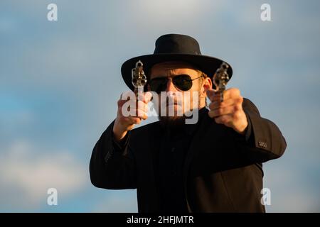 Sheriff in schwarzem Anzug und Cowboyhut mit Schießgewehr, Nahaufnahme Westerngesicht. Sheriff oder Cowboy in schwarzem Anzug und Cowboyhut. Mann mit Westernpistole Stockfoto