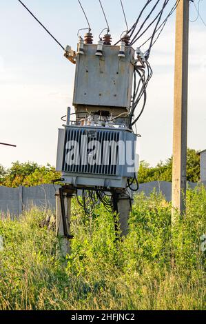 Elektrischer Transformator auf dem Feld hinter dem Dorf, Drähte und ein Pol. Elektrogeräte im alten Stil. Stockfoto