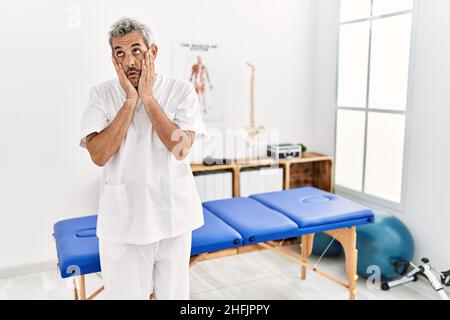 hispanischer Therapeut im mittleren Alter, der in der Schmerzklinik arbeitet, müde Hände, die Gesicht, Depression und Traurigkeit bedecken, aufgeregt und wegen des Problems verärgert sind Stockfoto