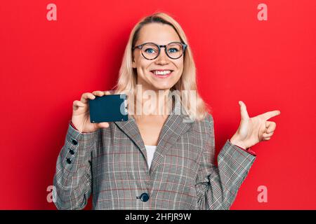 Schöne kaukasische blonde Geschäftsfrau hält ssd-Speicher lächelnd glücklich zeigt mit Hand und Finger zur Seite Stockfoto