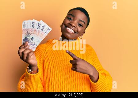 Junge afroamerikanische Frau mit isländischen Kronen-Banknoten lächelnd und mit Hand und Finger zeigend Stockfoto