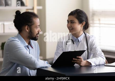 Lächelnder, tausendjähriger indischer Arzt, der die Testergebnisse mit dem Patienten diskutiert. Stockfoto
