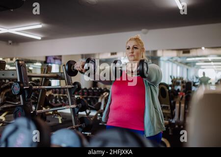 Plus size Frau Training und Heben Hanteln drinnen im Fitnessstudio Stockfoto