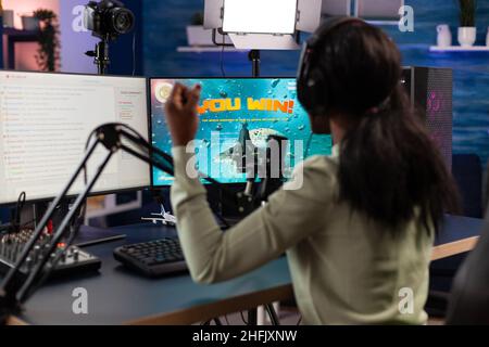 Aufgeregt glücklich esport Frau spielen Online-Videospiele gewinnen Weltraum-Shooter-Turnier. Erfolgreicher Spieler, der im Heimstudio mit Remote-Playern über die RGB-Tastatur spricht Stockfoto