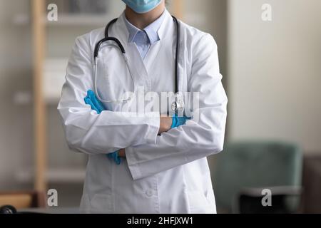 Beschnittenes Bild junge Ärztin, die mit gefalteten Armen steht. Stockfoto