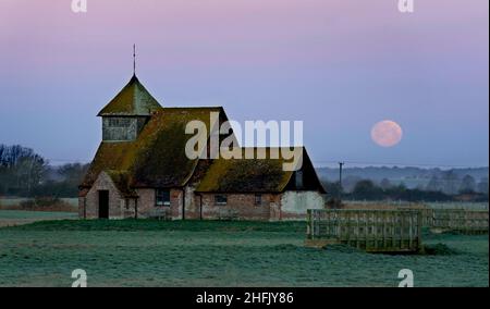 Der Mond untergeht hinter der St. Thomas Becket Kirche in Fairfield, Kent. Der erste Vollmond des Jahres 2022 - der Wolfmond, so die nordamerikanischen Ureinwohner - ist Montagabend. Bilddatum: Montag, 17. Januar 2022. Stockfoto