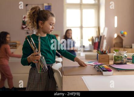 Glückliches kleines Mädchen mit ihren Freunden, die sich in der Schule für Kunst- und Handwerksklasse vorbereiten Stockfoto