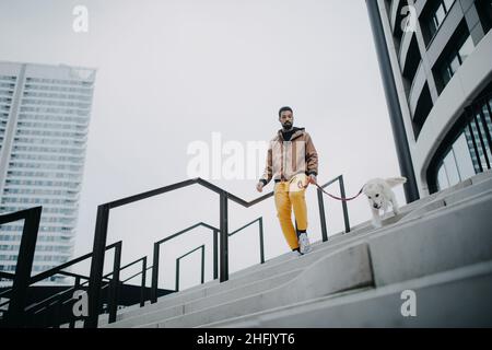 Blick aus der unteren Ecke auf einen jungen Mann, der seinen Hund im Freien in der Stadt nach unten läuft. Stockfoto